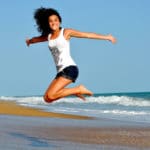 woman smiling and jumping on beach