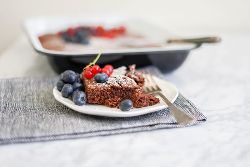 horizontal picture of a close-up brownie on a plate with fresh blueberries