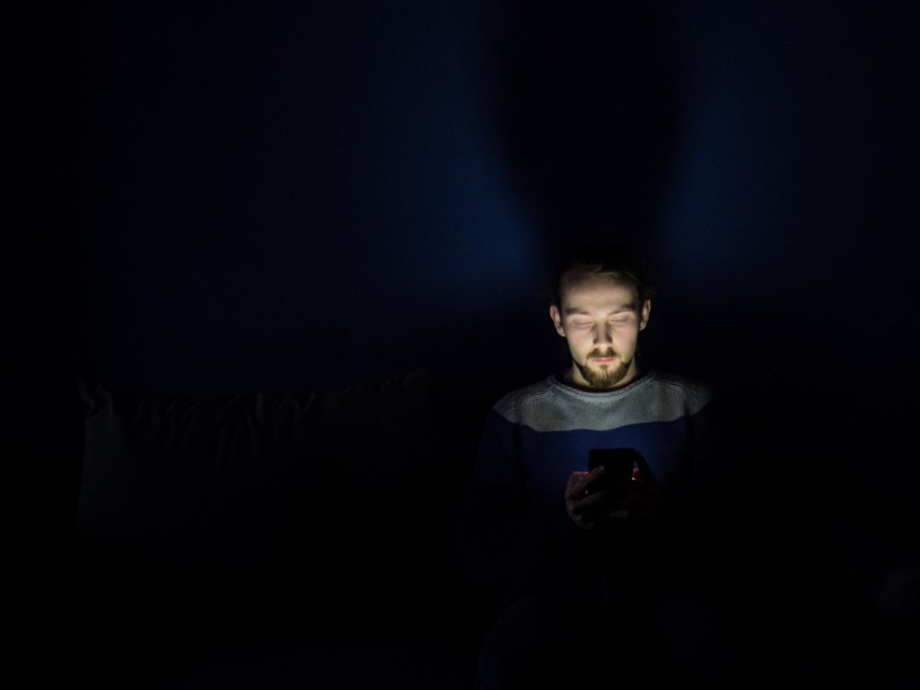 A man in the dark with his face illuminated by an electronics screen