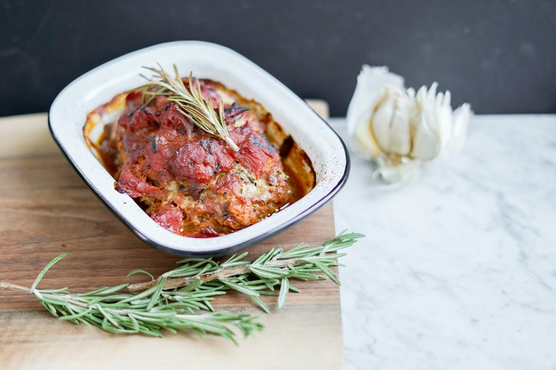 a mini meatloaf in a white enamel container with fresh rosemary around