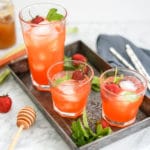 eye-level view of 3 glasses of strawberry rhubarb lemonade on a metal tray with fresh strawberries