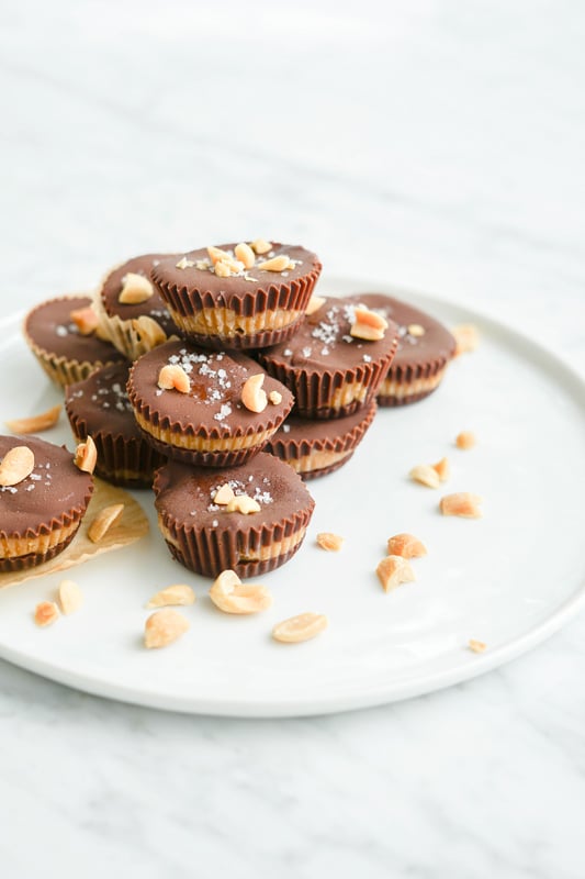 Close-up eye-level view of several homemade peanut butter cups on a white plate with peanuts around