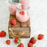 horizontal view of strawberry yogurt jars on a small wood box on a white marble table
