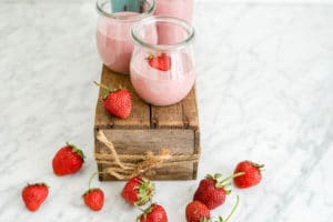 horizontal view of strawberry yogurt jars on a small wood box on a white marble table