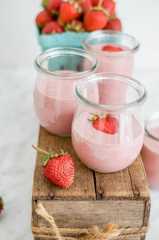 close-up view of vegan strawberry yogurt in 3 small glass jars on top of a wooden box