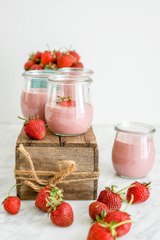 front view of vegan strawberry yogurt in small glass containers on top of a wood box with fresh strawberries in front