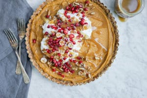 Top-down view of a no bake pumpkin pie with coconut whipped cream on top and sprinkled with chopped pecans and pomegranate