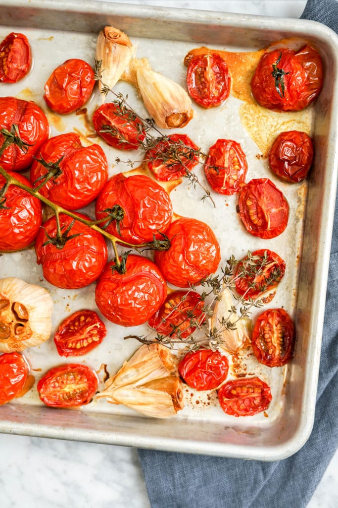 cooked tomatoes on vine and garlic in a sheet pan