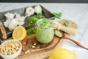 horizontal view of pesto with ingredients scattered on a wood cutting board on a marble table