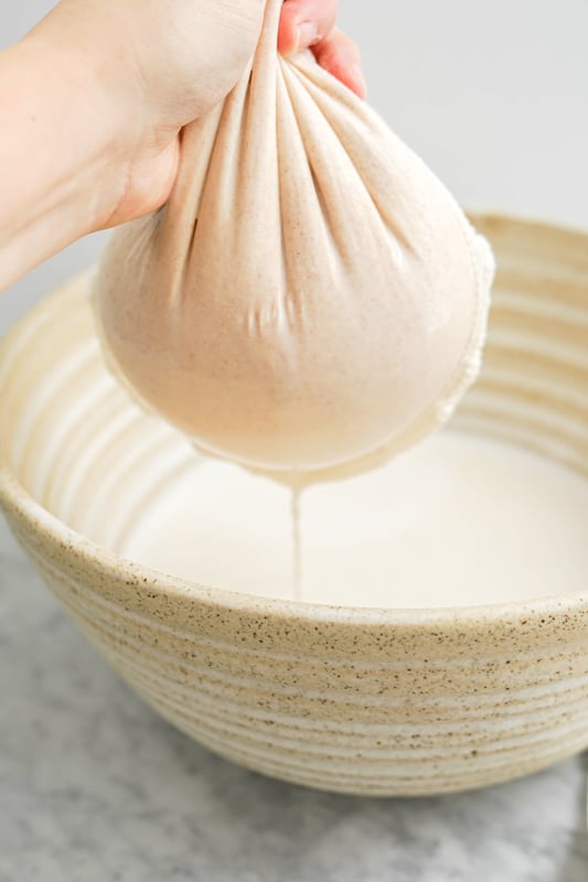 a hand squeezing a nut milk filter over a large bowl with milk dripping in it
