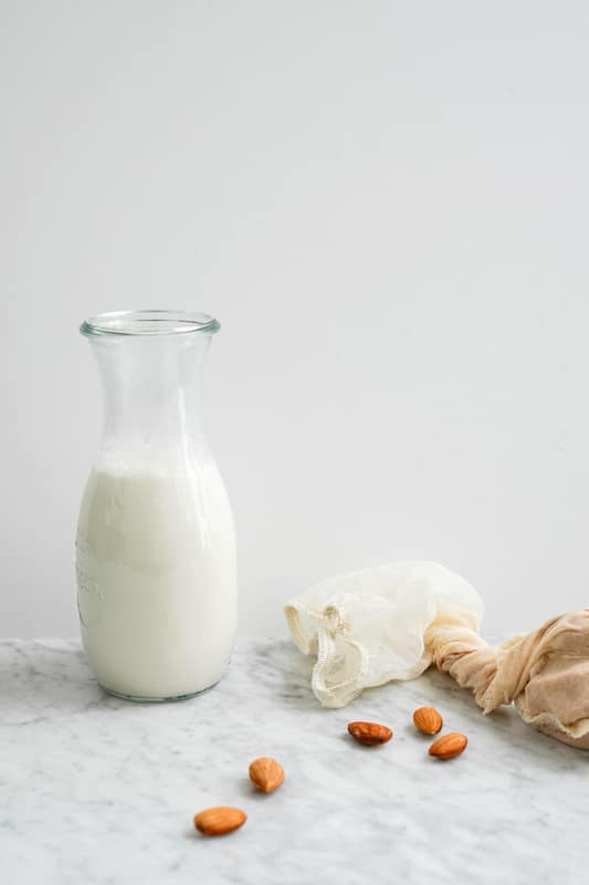 a large clear glass bottle full of almond milk with whole almonds on the side