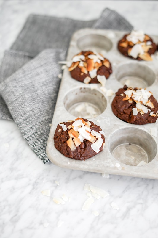 front view of a few chocolate muffins with coconut flakes on top in a muffin tin