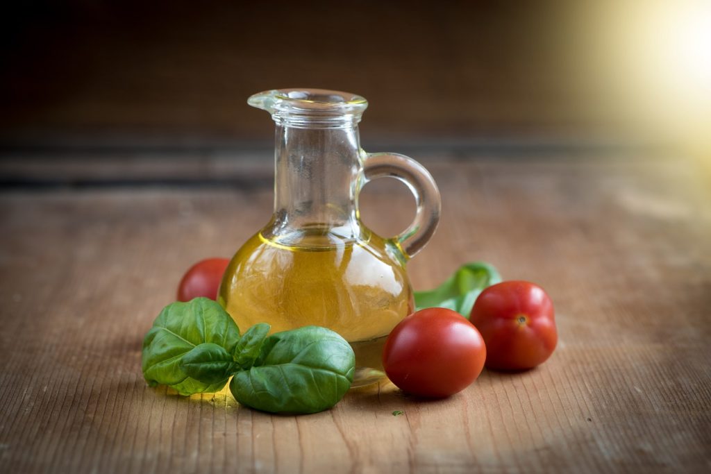 A small clear glass pitcher of olive oil with cherry tomatoes around it