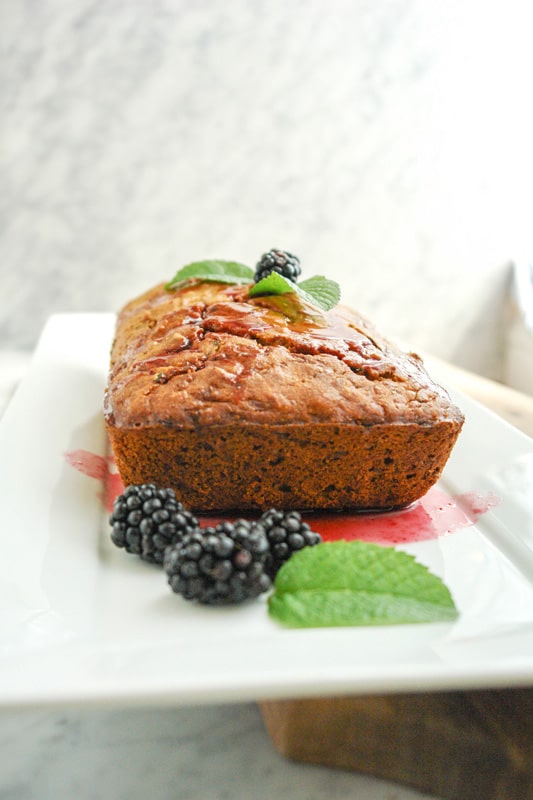 a Lemon Zucchini Bread with blackberries and mint leaves on a rectangular white plate on top of white marble