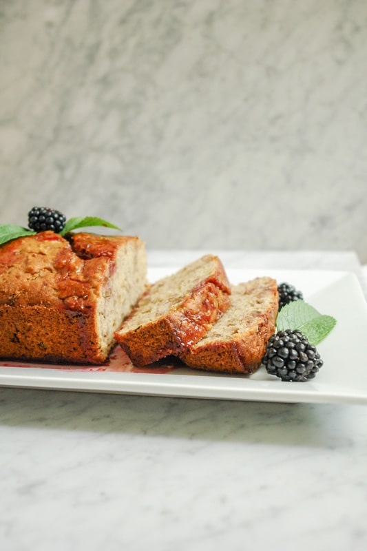 a Lemon Zucchini Bread with blackberries and mint leaves on a rectangular white plate on top of white marble