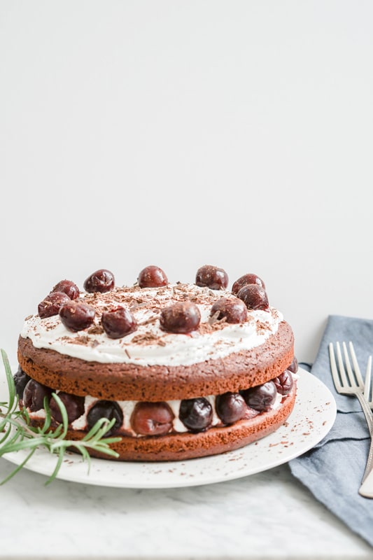 a simple healthy chocolate cake with coconut cream and cherries on a white background