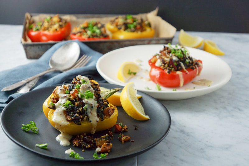 quinoa and roasted vegetable-stuffed yellow and red peppers in a black and white plates with more stuffed peppers in background