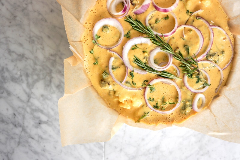 aerial view of the cauliflower cake before being baked, with round slices of raw red onions and a fresh rosemary sprig on top