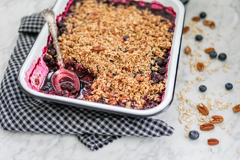 horizontal view of baked apple blueberry crumble with a spoon in it and oat flakes on the side