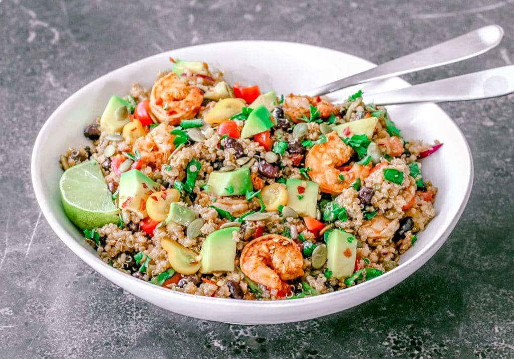 Front view close-up of a white bowl with quinoa, avocado cubes and shrimp salad